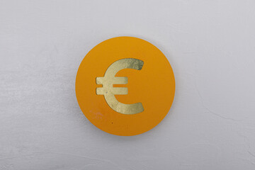 A close-up of a golden euro symbol on a yellow circle against a grey wall, representing European finances and the monetary system.