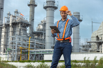 Asian industrial engineer wearing safety helmet and holding digital tablet while inspecting power plant, representing smart industry, digital engineering and occupational safety.