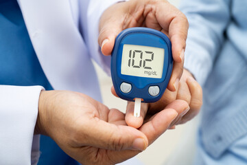 Asian doctor using digital glucose meter for check sample blood sugar level to treatment diabetes.