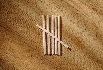 Wooden sticks are arranged to form the tally mark for the number five. Set against textured hardwood surface. The scene is lit by strong directional light, creating deep shadows.