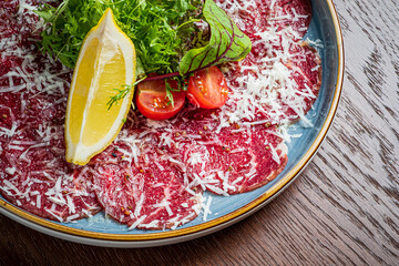 Savor the flavors of tender carpaccio garnished with fresh greens and zesty lemon slices