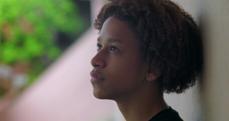 One Hispanic young boy of African descent with curly hair, looking up, deep in thought outdoors,...