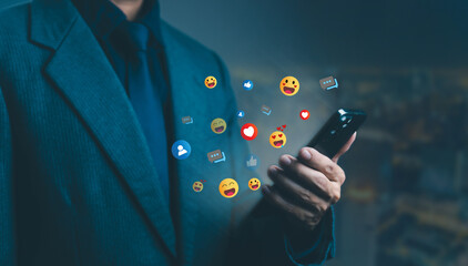 A businessman using a smartphone with social media reaction icons such as like, heart, and emoji floating around, representing online communication, digital marketing, and social media engagement.