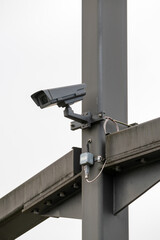 Close up on a surveillance camera on a massive mast, against a grey sky. Vertical shot.