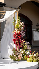 Colorful wedding romantic flower arch with white fabric. Summer atmosphere on the street. Green white and red flowers. Rose, hydrangea, anthurium, dahlia, chrysanthemum, amaranth, dianthus white spray