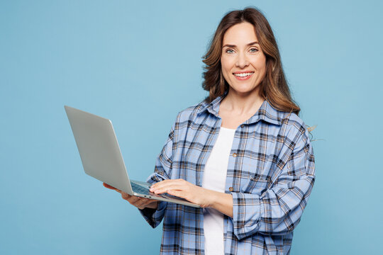Young smart IT woman she wears checkered shirt casual clothes hold use work on laptop pc computer typing message isolated on plain pastel light blue cyan background studio portrait. Lifestyle concept.