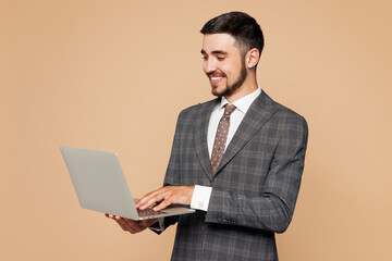 Young smiling smart fun employee IT business man corporate lawyer wear classic formal grey suit shirt tie work in office hold use laptop pc computer isolated on plain beige background studio portrait.