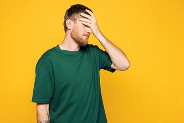 Young shocked Caucasian man he wear green t-shirt casual clothes put hand on face facepalm epic fail mistaken omg gesture isolated on plain yellow orange background studio portrait. Lifestyle concept.