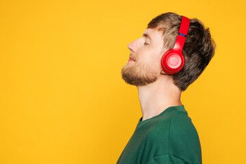Side view young Caucasian man he wearing green t-shirt casual clothes listen to tranquil music in headphones close eyes isolated on plain yellow orange background studio portrait. Lifestyle concept.