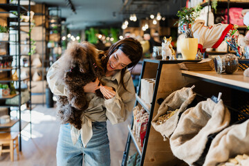 Woman holding a cute brown mini poodle and selecting high-quality pet food and treats in a modern...