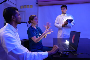 group of two male and one female doctors of various nationalities sat in a meeting, debated, and the male doctor presented his work in a conference room and studied research data on treating patients 