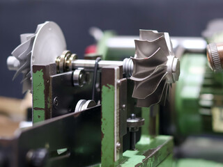 Turbocharger rotor assembly, featuring both the compressor and turbine wheels on a central shaft, mounted on a green balancing or inspection machine.