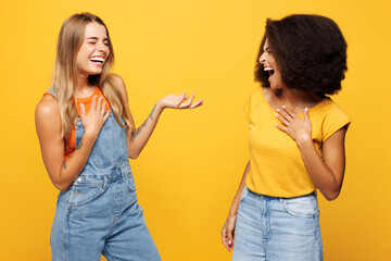 Two young cheerful friends buddies women wearing denim casual clothes talk speak have fun conversation laughing together isolated on plain yellow orange background studio portrait. Lifestyle concept.