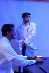 group of doctors is having a treatment planning meeting and a handsome Caucasian male doctor presents at the front of the room, discussing research data with slides on the wall.