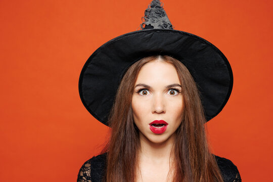Fototapeta Close up young shocked surprised woman wearing black hat dress witch costume posing looking camera isolated on plain red orange background studio portrait. Celebration Halloween holiday party concept.