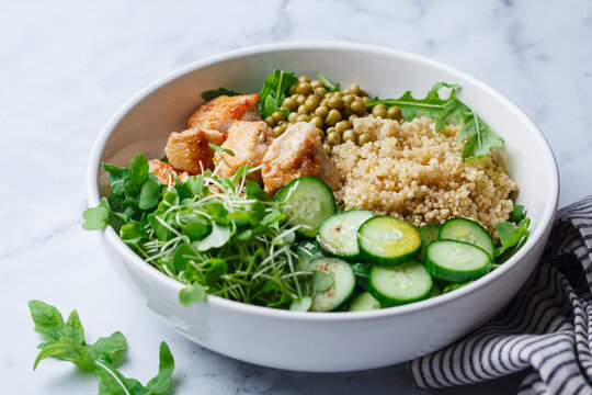 Balanced quinoa, arugula, chicken, cucumber and pea lunch bowl.
