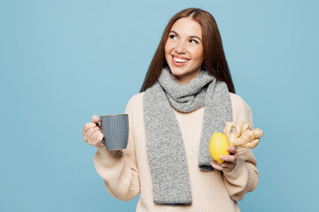 Young woman wear pink sweater scarf hold cup lemon ginger drink tea look aside area isolated on plain blue background studio portrait. Healthy lifestyle ill sick disease treatment cold season concept.