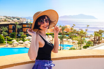 A girl in a hat and glasses on a terrace with a gorgeous view of the sea, mountains and palm trees.