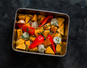 Ingredients for making pumpkin soup - pumpkin, sweet pepper, onion, garlic, thyme, olive oil in a baking dish on a dark background