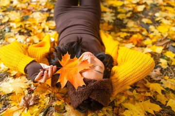 The Asian girl lies in the autumn leaves and holds out one to the camera, a good autumn photo of a teenager. Top view.