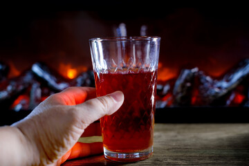 Red wine, Cherry and pomegranate juice in glass held by woman’s hand near fireplace in dark cozy room, warm light, autumn evening atmosphere, relaxation, romantic intimate mood, relaxation drink