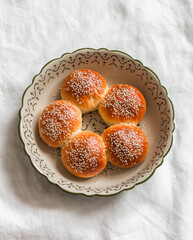 Sweet sesame buns in a baking dish on a light table, top view