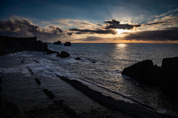Obraz premium Dramatic sunset over the ocean with rocky coastline, a stunning seascape for travel inspiration and coastal adventures, feel the tranquility of nature's beauty on a peaceful evening