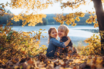 Siblings in autumn nature, sitting on fallen leaves.