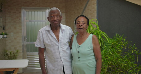 Elderly African American couple standing side by side outdoors, both looking at the camera with...
