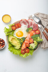 Healthy ketogenic diet concept showing a balanced meal on plate with salmon, avocado, fried egg, bacon, broccoli, tomato, and fresh salad, promoting low carb and high fat eating
