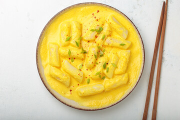 Delicious korean tteokbokki rice cakes served in a creamy cheese sauce, topped with green onion slices, presented in a bowl with chopsticks, authentic food of Korea