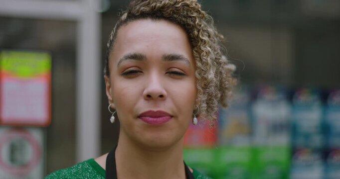 Close-up of a female shopkeeper with curly hair looking composed and focused while standing outdoors in front of a store