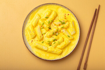 Delicious korean tteokbokki rice cakes served in a creamy cheese sauce, topped with green onion slices, presented in a bowl with chopsticks, authentic food of Korea