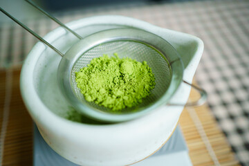 Woman sifting matcha powder into bowl on digital scale.