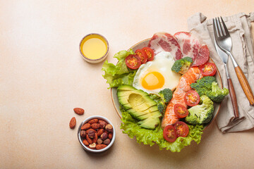 Healthy ketogenic diet concept showing a balanced meal on plate with salmon, avocado, fried egg, bacon, broccoli, tomato, and fresh salad, promoting low carb and high fat eating, copy space