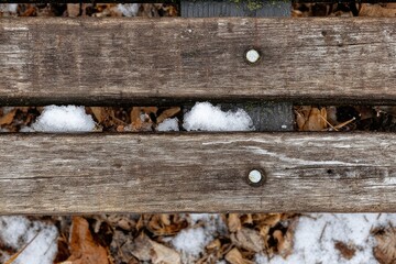 Overhead shot of weathered wooden park bench planks with snow and autumn leaves in between