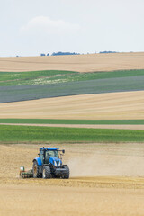 Fototapeta premium Blue tractor tilling field after harvest in France