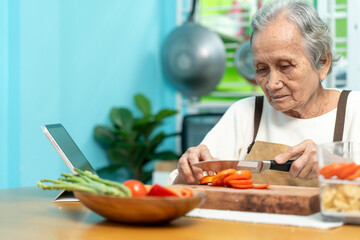 Elderly woman are cooking in their home kitchen and slicing tomatoes to prepare for salad.