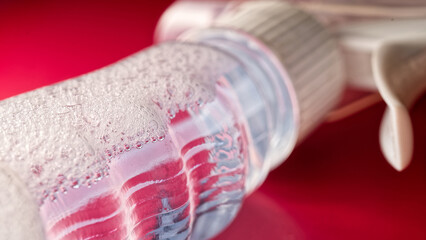 Close-up of a transparent spray bottle with foamy cleaning liquid and condensation on a red background, cleaning concept. Photo