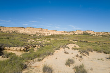 This landscape photo was taken in Europe, Spain, Navarre, in summer. It shows the green fields and cliffs in the Bardenas Reales, under the Sun.