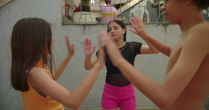 Children in courtyard playing rhythmic hand-clapping game, smiling, bonding, carefree fun, joyful energy, sibling interaction, creating happy childhood memories