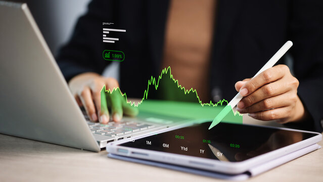 Businesswoman analyzing financial data with tablet and laptop showing green growth chart concept of stock market investment
