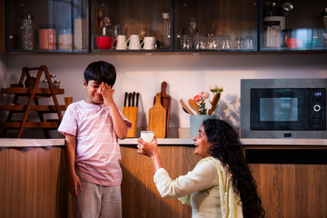 Indian Child refusing milk as caring mother explains health importance in modern home kitchen