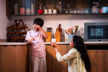 Indian Child refusing milk as caring mother explains health importance in modern home kitchen