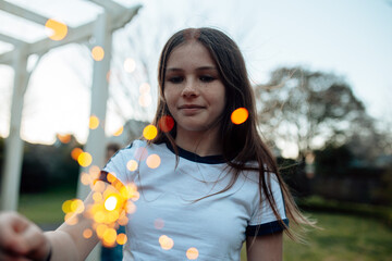 Young preteen girl holding a sparkler in the garden