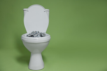 Dollar banknotes in toilet bowl on green background. Space for text
