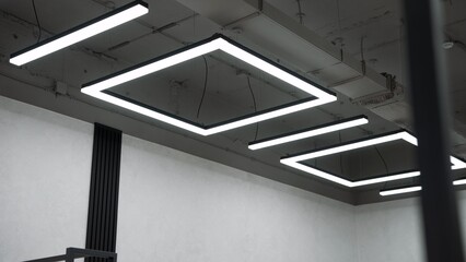 Contemporary office space displaying concrete ceiling and minimalist square led light fixtures,...