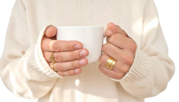 Close-up of hands holding a white mug, wearing rings, cozy sweater aesthetic