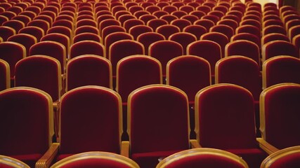 Rows of luxurious red velvet seats with golden accents filling an empty theatre or cinema auditorium, waiting for an audience