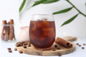 Tasty iced coffee in glass and beans on white table, closeup